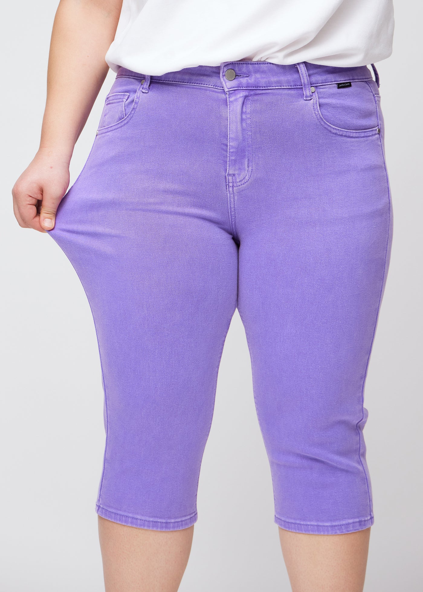 Plus-size model viser stretch ved at trække i caprisene ved låret – fokus på komfort og fleksibilitet.