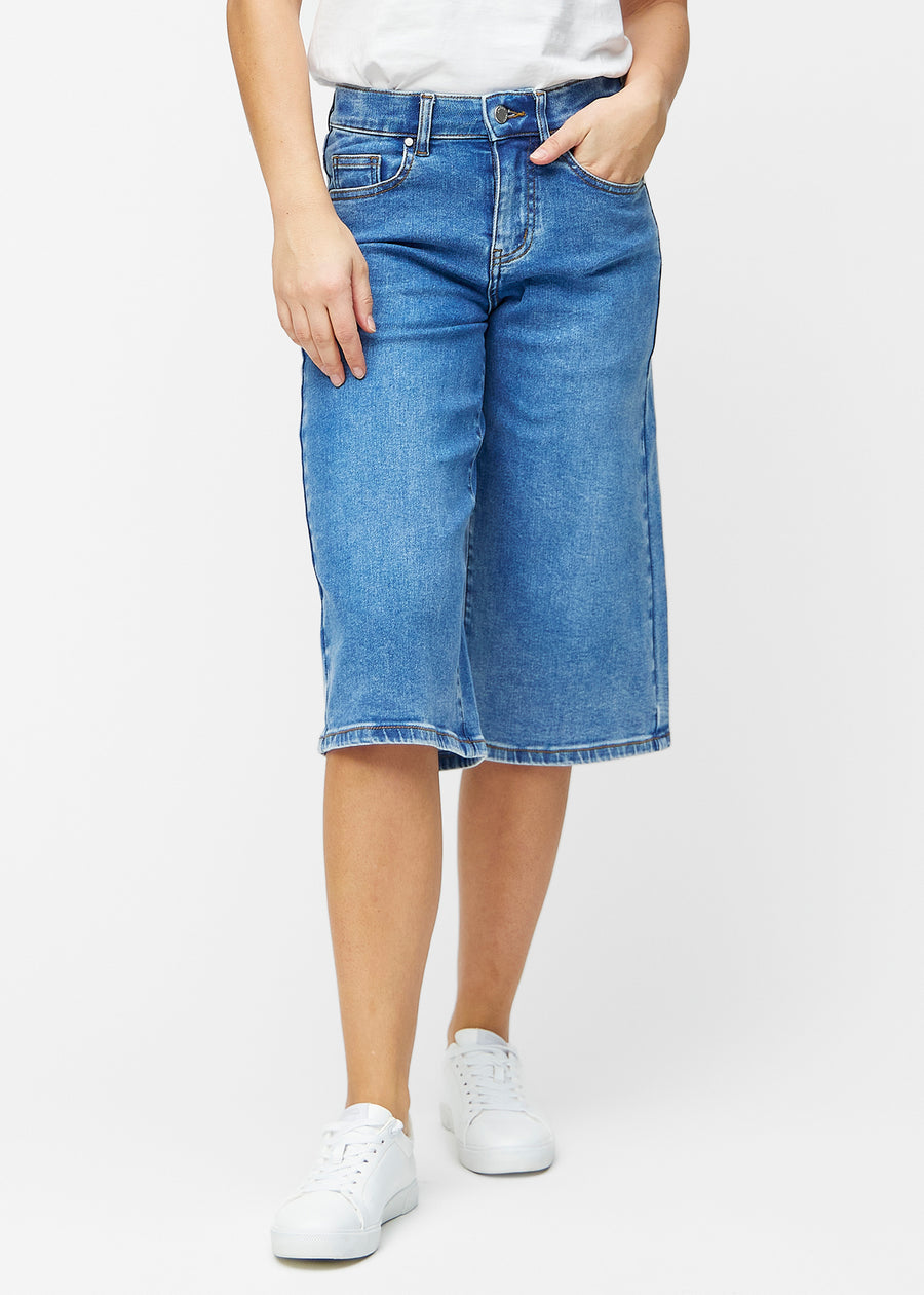 Løse, klassisk blå denim capris i farven Rivers, der sidder til ved hoften og falder løst ned over lårene til lige under knæet, set forfra.
