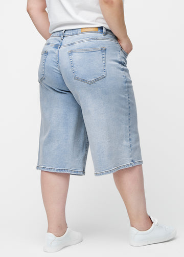 Lösa, ljusblå denim capris i färgen Waves sedda bakifrån på plus-size modell, så att passform och längd syns.