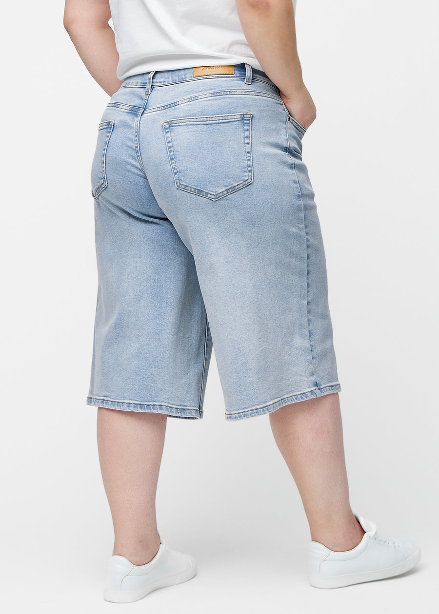 Lösa, ljusblå denim capris i färgen Waves sedda bakifrån på plus-size modell, så att passform och längd syns.
