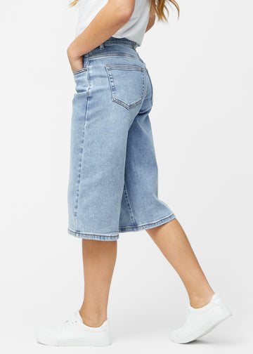 Lösa, ljusblå denim capris i färgen Waves sedda från sidan på modell, där den breda passformen och längden till precis under knät syns.
