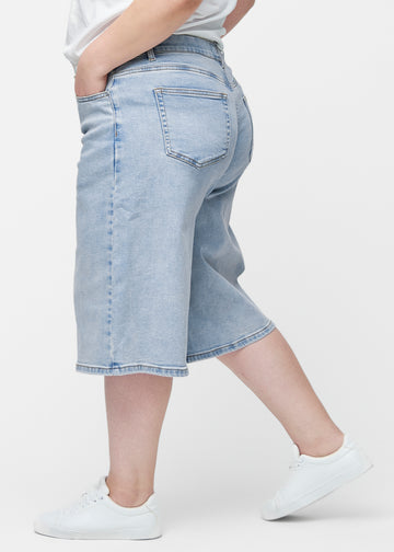 Lösa, ljusblå denim capris i färgen Waves sedda från sidan på plus-size modell, där den breda passformen och längden till precis under knät syns.