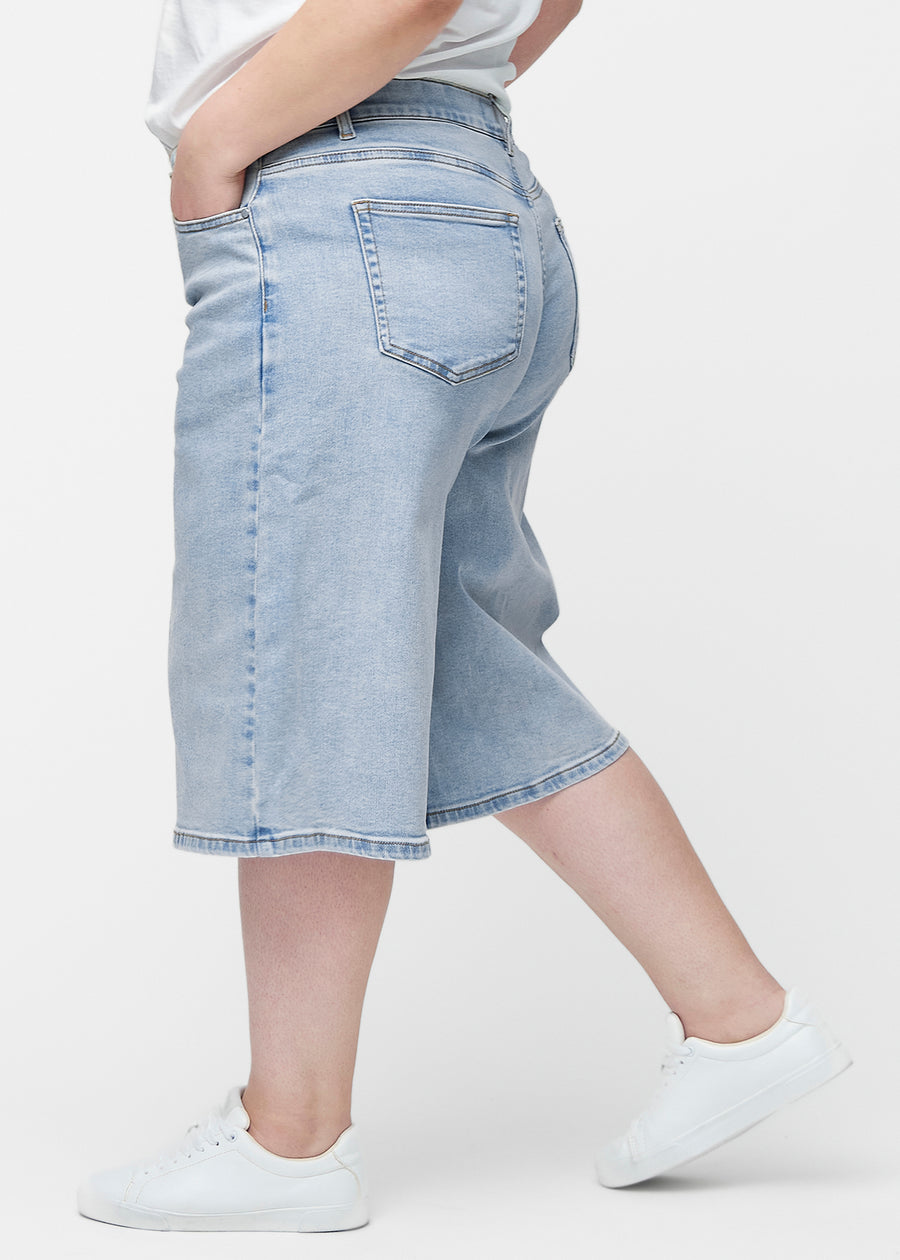 Lösa, ljusblå denim capris i färgen Waves sedda från sidan på plus-size modell, där den breda passformen och längden till precis under knät syns.