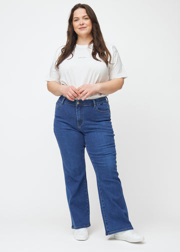 Mörkblå mid-rise bootcutjeans i färgen Oceans. Helbild av en plus size-modell i jeansen.
