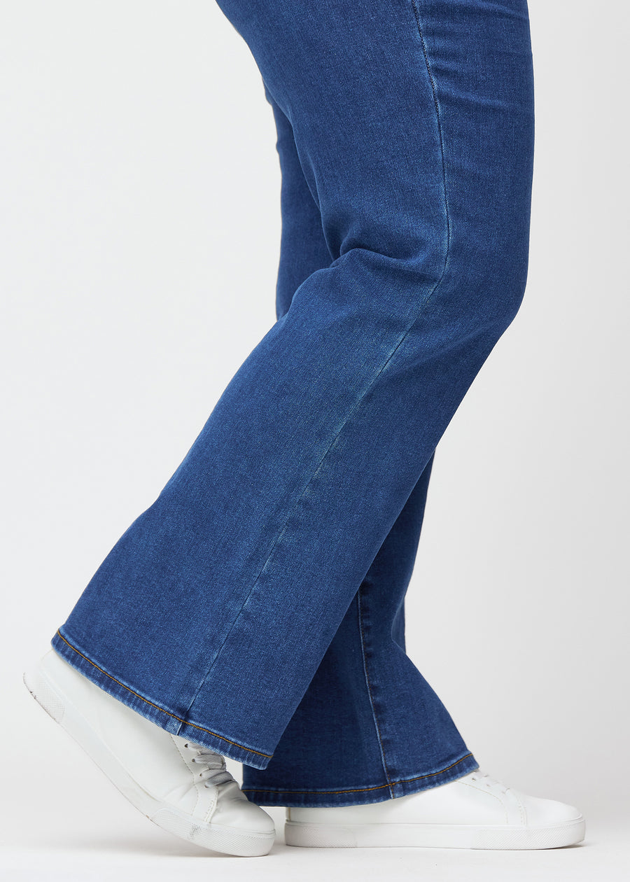Mörkblå mid-rise bootcutjeans i färgen Oceans. Närbild vid ankeln på en plus size-modell som visar den lätta utsvängningen nedtill.