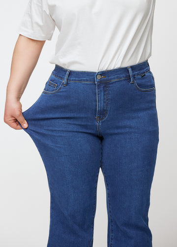 Mörkblå mid-rise bootcutjeans i färgen Oceans. En plus size-modell drar i jeanstyget vid låret för att visa stretchen.