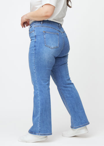 Blå mid-rise bootcutjeans i färgen Rivers. Från sidan på en plus size-modell.