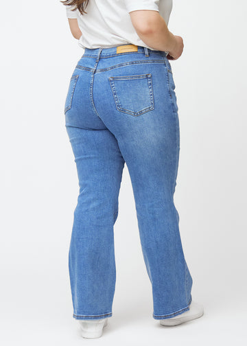 Blå mid-rise bootcutjeans i färgen Rivers. Bakifrån på en plus size-modell, så att hela passformen syns.