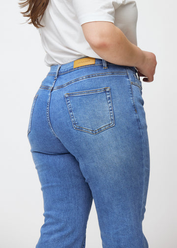 Blå mid-rise bootcutjeans i färgen Rivers. Närbild bakifrån på en plus size-modell som visar detaljerna.