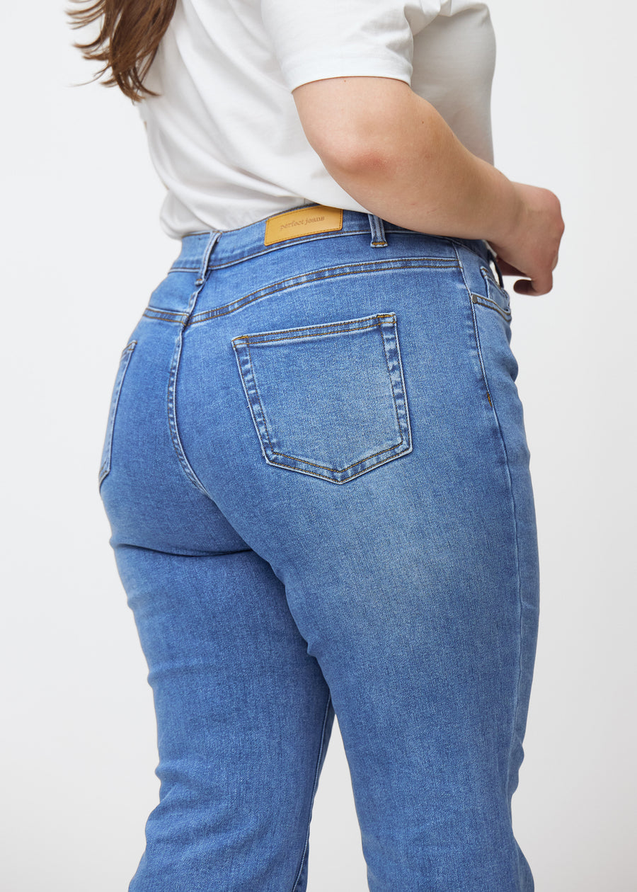 Blå mid-rise bootcutjeans i färgen Rivers. Närbild bakifrån på en plus size-modell som visar detaljerna.