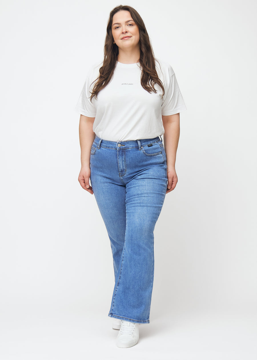 Blå mid-rise bootcutjeans i färgen Rivers. Helbild av en plus size-modell i jeansen.