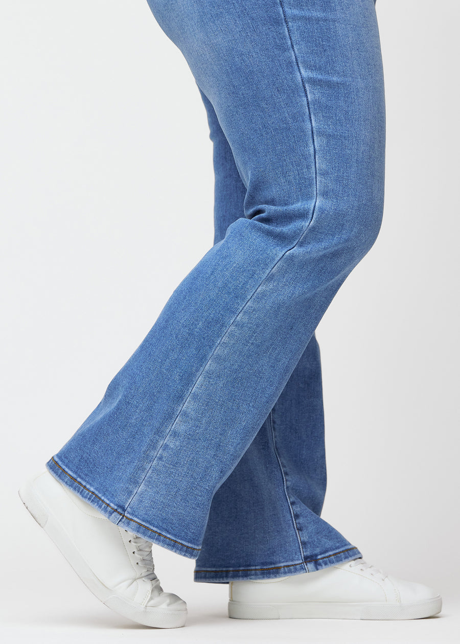 Blå mid-rise bootcutjeans i färgen Rivers. Närbild vid ankeln på en plus size-modell som visar den lätta utsvängningen nedtill.
