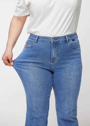 Blå mid-rise bootcutjeans i färgen Rivers. En plus size-modell drar i jeanstyget vid låret för att visa stretchen.