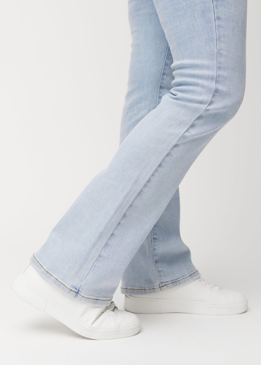 Ljusblå mid-rise bootcutjeans i färgen Waves. Närbild vid ankeln på en modell som visar den lätta utsvängningen nedtill.