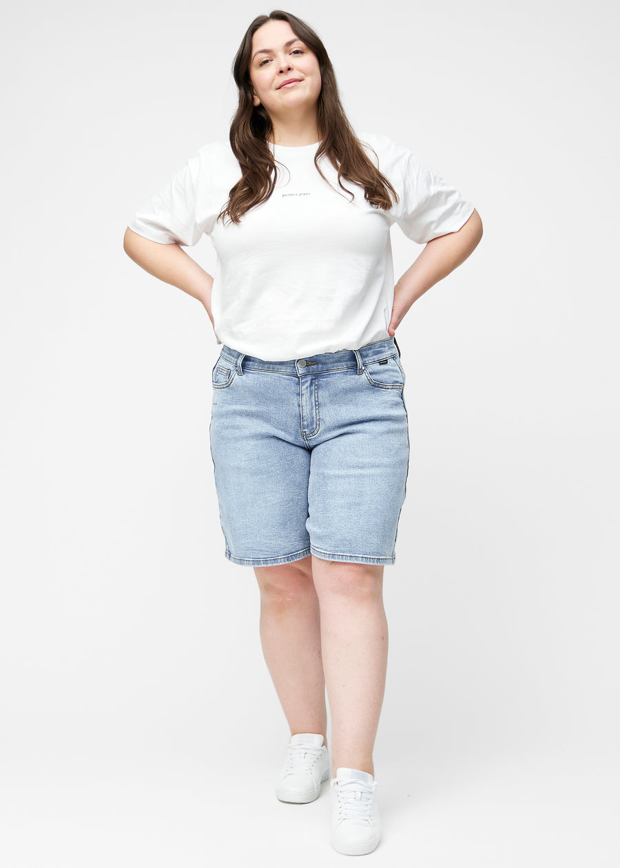 Helbild av plus-size modell i lösa, ljusblå denimshorts i färgen Waves som går till precis över knät.