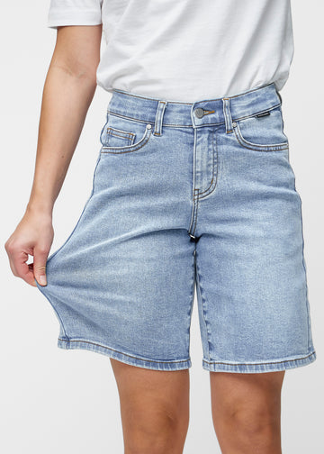 Lösa, ljusblå denimshorts i färgen Waves som sitter vid höften och faller löst över låren till precis över knät, sett framifrån.
