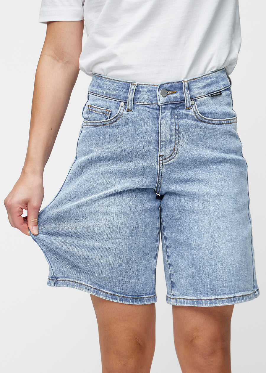 Lösa, ljusblå denimshorts i färgen Waves som sitter vid höften och faller löst över låren till precis över knät, sett framifrån.
