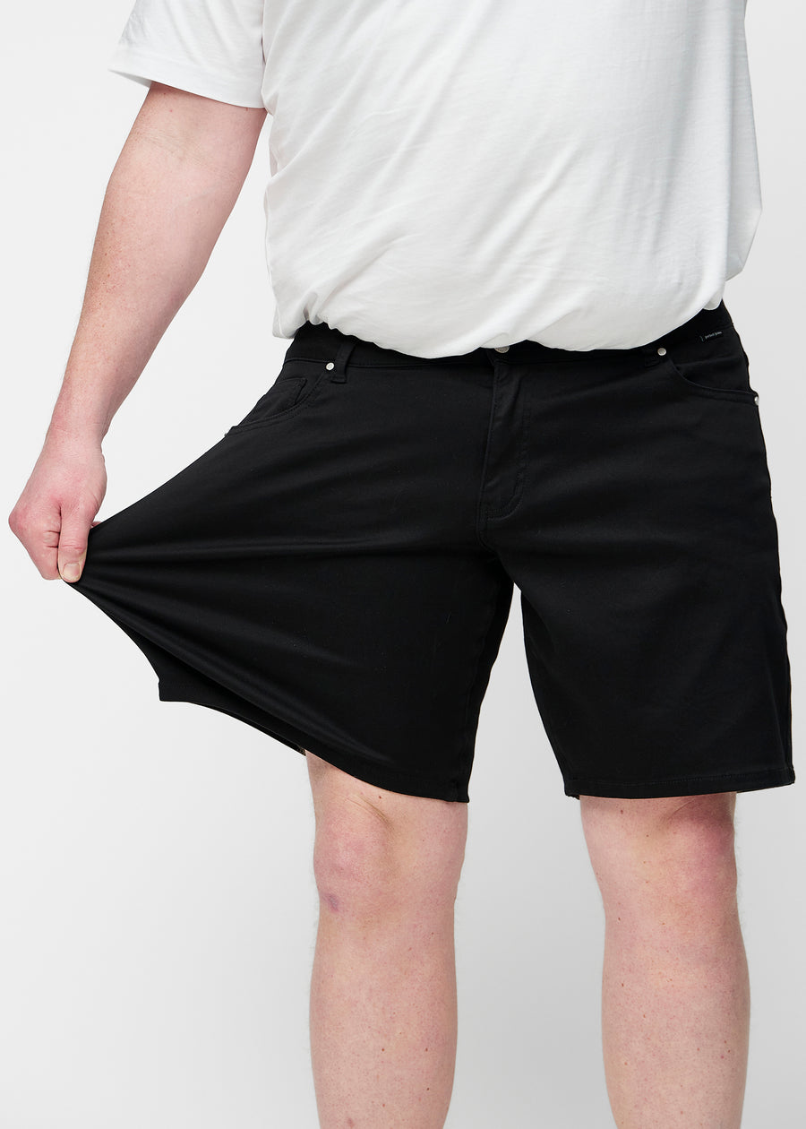 Plus-size modell sträcker svarta shorts för herr i färgen Ravens vid låret för att visa materialets stretch.