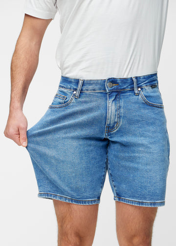Modell sträcker blå denimshorts för herr i färgen Rivers vid låret för att visa materialets stretch.