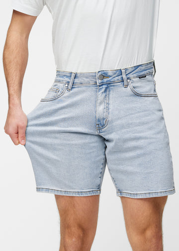 Modell sträcker ljusblå denimshorts för herr i färgen Waves vid låret för att visa materialets stretch.