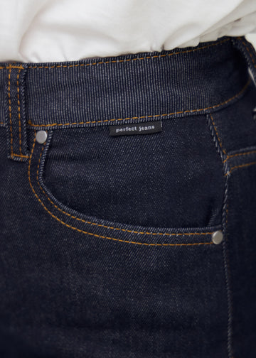 Närbild av mörkblå denim med Perfect Jeans logomärke vid framfickan.