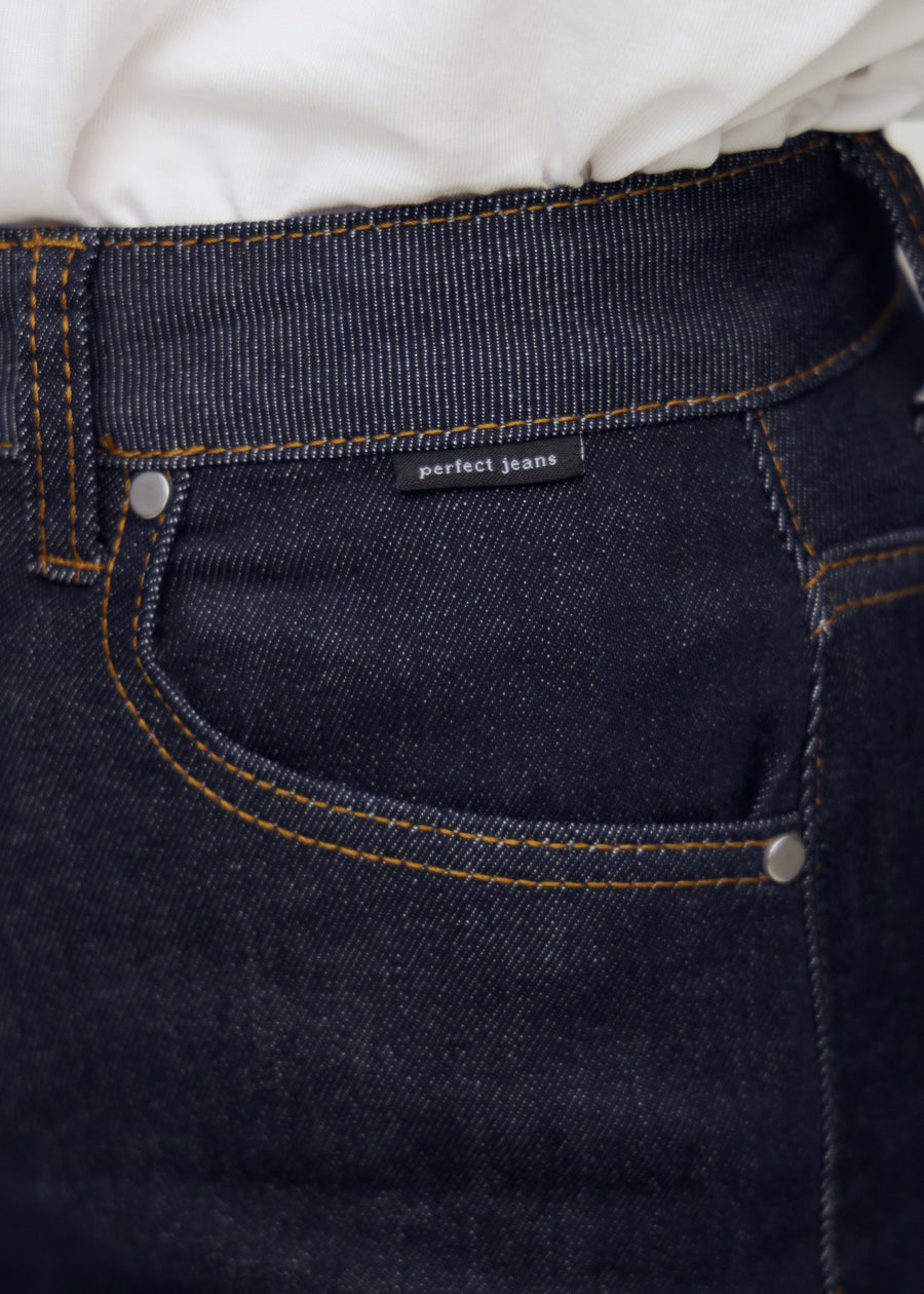 Närbild av mörkblå denim med Perfect Jeans logomärke vid framfickan.