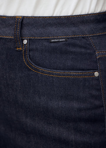 Närbild av mörkblå denim med Perfect Jeans logomärke vid framfickan på plus-size modell.