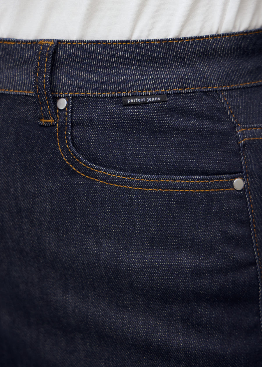 Närbild av mörkblå denim med Perfect Jeans logomärke vid framfickan på plus-size modell.
