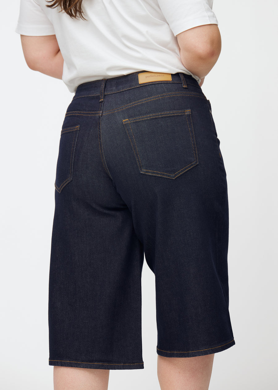 Mörkblå denim capris för dam i färgen Midnights sett bakifrån i närbild på plus-size modell.