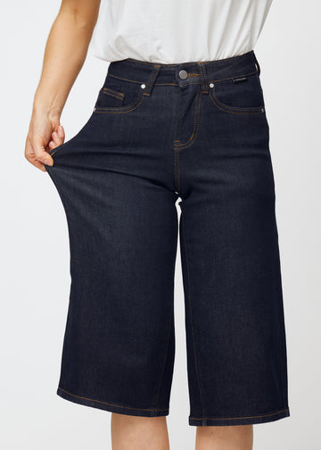 Modell sträcker mörkblå denim capris för dam i färgen Midnights vid låret för att visa materialets stretch.