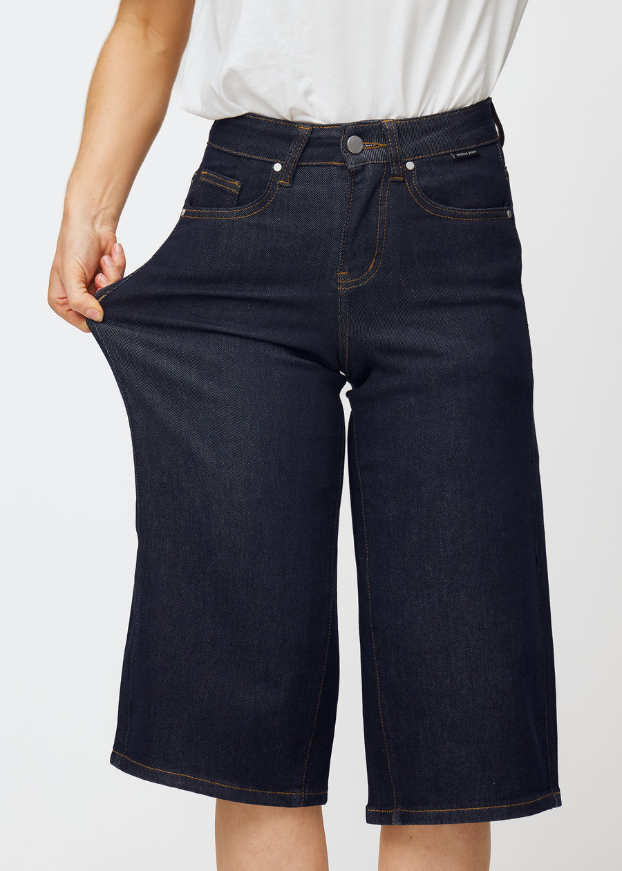 Modell sträcker mörkblå denim capris för dam i färgen Midnights vid låret för att visa materialets stretch.
