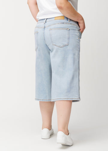 Lösa, ljusblå Waves denimcapribyxor sedda bakifrån på en plus-size-modell för att visa passform och längd.