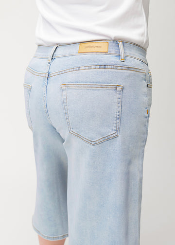 Närbild bakifrån av lösa, ljusblå Waves denimcapribyxor på en plus-size-modell som visar passform och detaljer.