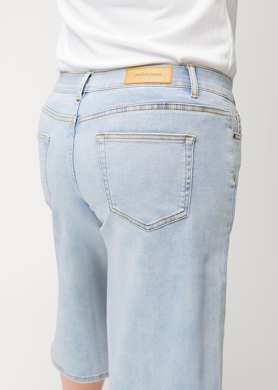 Närbild bakifrån av lösa, ljusblå Waves denimcapribyxor på en plus-size-modell som visar passform och detaljer.