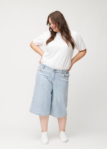 Helbild av en plus-size-modell i lösa, ljusblå Waves denimcapribyxor som slutar strax nedanför knät.