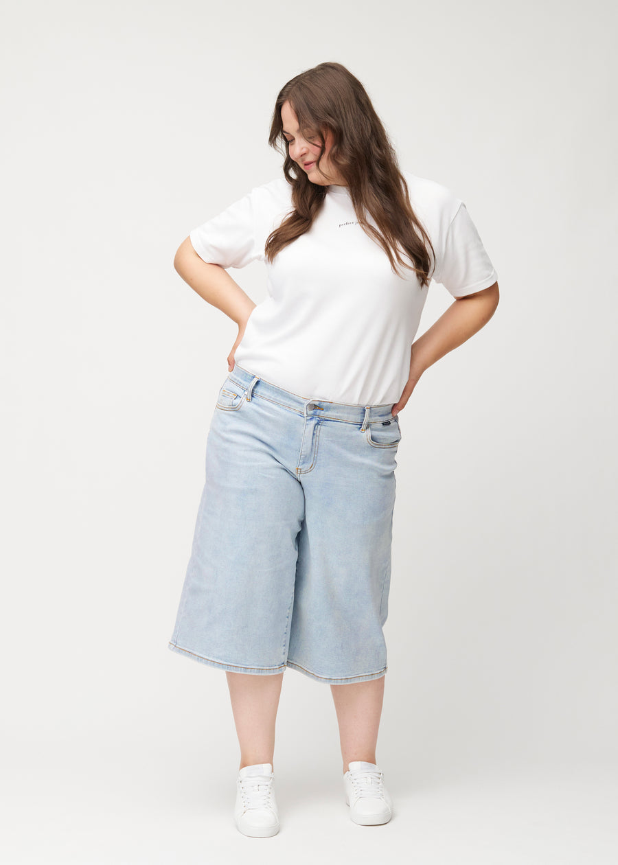 Helbild av en plus-size-modell i lösa, ljusblå Waves denimcapribyxor som slutar strax nedanför knät.
