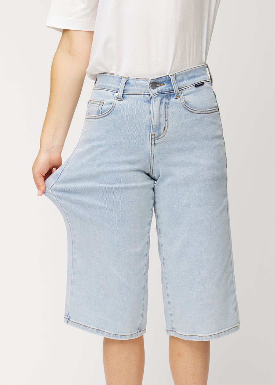 Modell drar i de lösa, ljusblå Waves denimcapribyxorna vid höften för att visa materialets stretch.