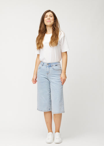 Helbild av en modell i lösa, ljusblå Waves denimcapribyxor som slutar strax nedanför knät.