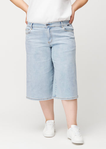 Plus-size-modell sedd framifrån i lösa, ljusblå Waves denimcapribyxor som sitter åt vid höfterna och faller löst.