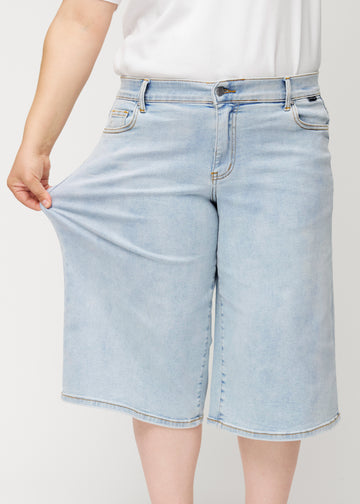 Plus-size-modell drar i de lösa, ljusblå Waves denimcapribyxorna vid höften för att visa materialets stretch.