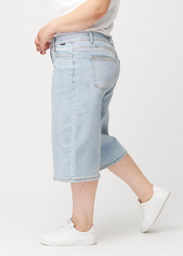 Lösa, ljusblå Waves denimcapribyxor sedda från sidan på en plus-size-modell, som visar den vida passformen och längden till strax nedanför knät.