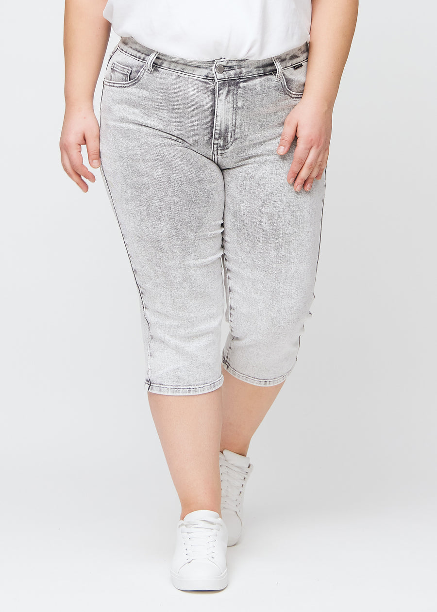 Ljusgrå denim regular capris, modellnamn Ashes, som sitter rakt längs benet och slutar precis under knät på en plus-size-modell, sedd framifrån.