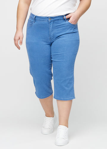 Blå regular capris, modellnamn Geraniums, som sitter rakt längs benet och slutar strax under knät på en plus-size-modell, sedda framifrån.