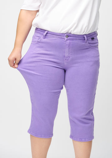 Plus size-modellen sträcker ut capribyxorna vid låret för att visa stretchen.