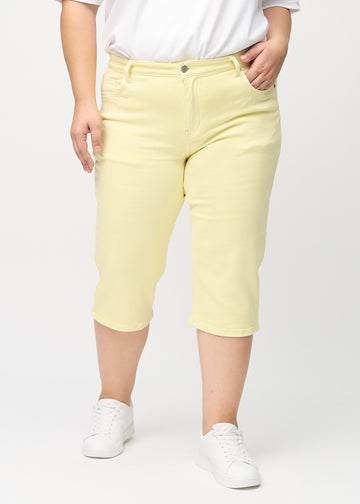Ljusgula regular capris, modellnamn Lemonades, som går rakt ner längs benet på en plus size-modell, framifrån.