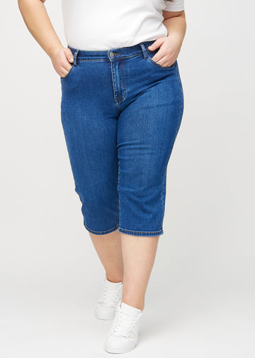 Mörk denim regular capris, modellnamn Oceans, som sitter rakt längs benet och slutar precis under knät på en plus size-modell, sett framifrån.