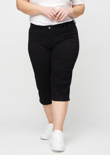 Svarta regular capris, modellnamn Ravens, som sitter rakt längs benet och slutar precis under knät på en plus-size-modell, sett framifrån.