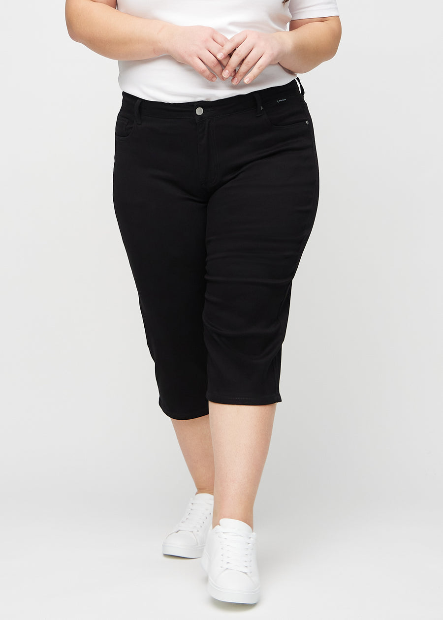 Svarta regular capris, modellnamn Ravens, som sitter rakt längs benet och slutar precis under knät på en plus-size-modell, sett framifrån.