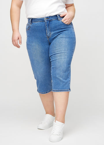 Denim regular capris, modellnamn Rivers, som sitter rakt längs benet och slutar strax under knät på en plus size-modell, framifrån.