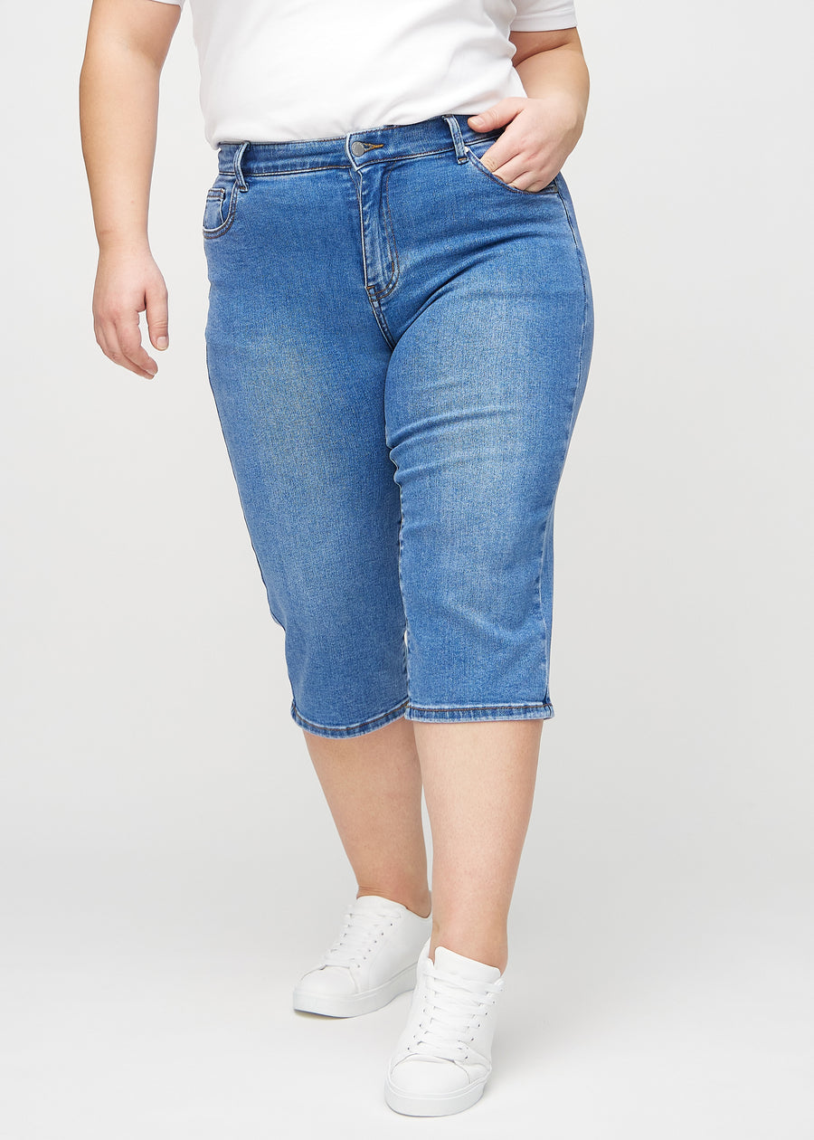 Denim regular capris, modellnamn Rivers, som sitter rakt längs benet och slutar strax under knät på en plus size-modell, framifrån.